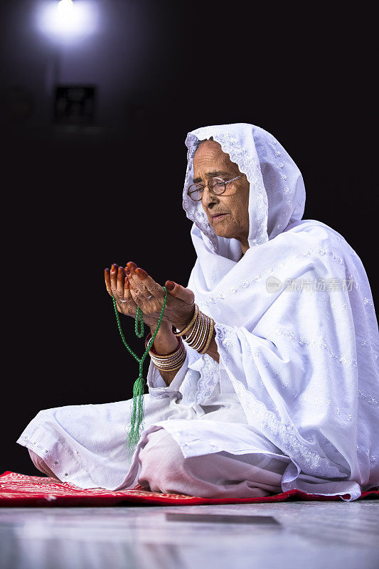 Senior Muslim Woman praying, with prayer beads beads in her hands